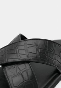 Sandales noires avec un motif crocodile embossé sur de larges brides, dotées d'une finition lisse et de semelles plates pour le confort.