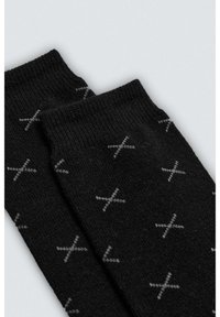 Calcetines tejidos de color negro con un patrón de formas 'X' en gris claro. Textura suave con un puño acanalado en la parte superior.