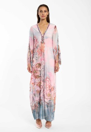 Frau steht und trägt ein langes, pastellfarbenes Blumenmusterkleid mit Perlenverzierung am V-Ausschnitt und geteilten Ärmeln, kombiniert mit hellrosa spitzen Absätzen.
