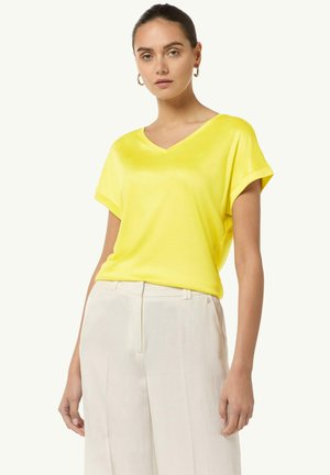 Yellow V-neck T-shirt made of lightweight fabric with rolled short sleeves, paired with light-colored wide-leg trousers. Clean design.