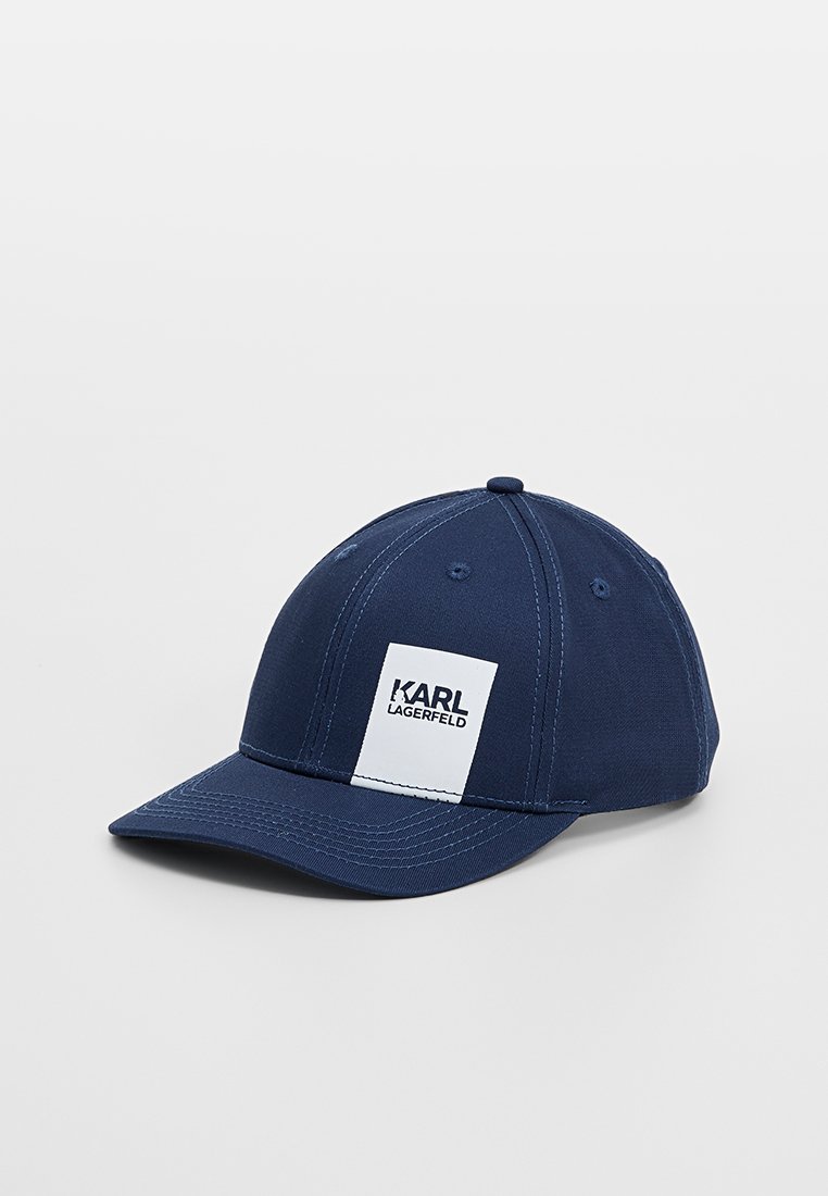 Casquette de baseball bleu marine en tissu avec une visière courbée, ornée d'un patch rectangulaire blanc embossé avec "KARL LAGERFELD". Design simple.