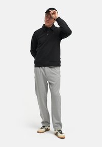 Schwarzes Langarmpolo mit diagonaler Gestaltung, graue Jogginghose und beige Sneakers. Das Modell passt eine schwarze Kappe an. Einfacher, lässiger Stil.