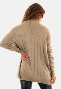 Pull beige à côtes avec une coupe décontractée, des épaules tombantes et des fentes sur les côtés. La texture tricotée et les manches longues complètent les tenues décontractées.