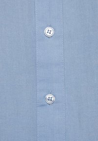 Light blue linen shirt featuring two silver buttons on the placket, characterized by a textured fabric and fine weave pattern.