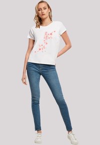 White t-shirt with short sleeves, featuring pink floral design and Japanese text. Worn with blue denim jeans and white sneakers.