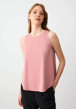 Top senza maniche di colore rosa con scollatura rotonda, tessuto morbido e orlo leggermente curvato, indossato con pantaloni neri.