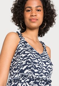 Vestido com padrão azul-marinho e branco, com alças com volantes e cintura ajustada, apresentando um decote em V em um tecido leve.
