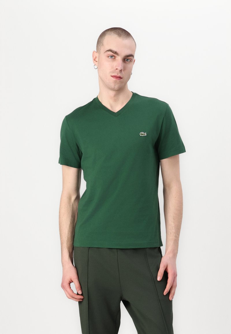 Zelené tričko s krátkým rukávem a výstřihem do V vyrobené z měkké bavlny. Na levé části hrudi je malé logo Lacoste. Nosit s odpovídajícími zelenými kalhotami.