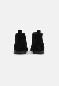 Botine din suede negru, la gleznă, cu un finisaj neted, cu bucle de tragere și un tocul mic. Designul include un vârf rotunjit și detalii de cusătură subtile.