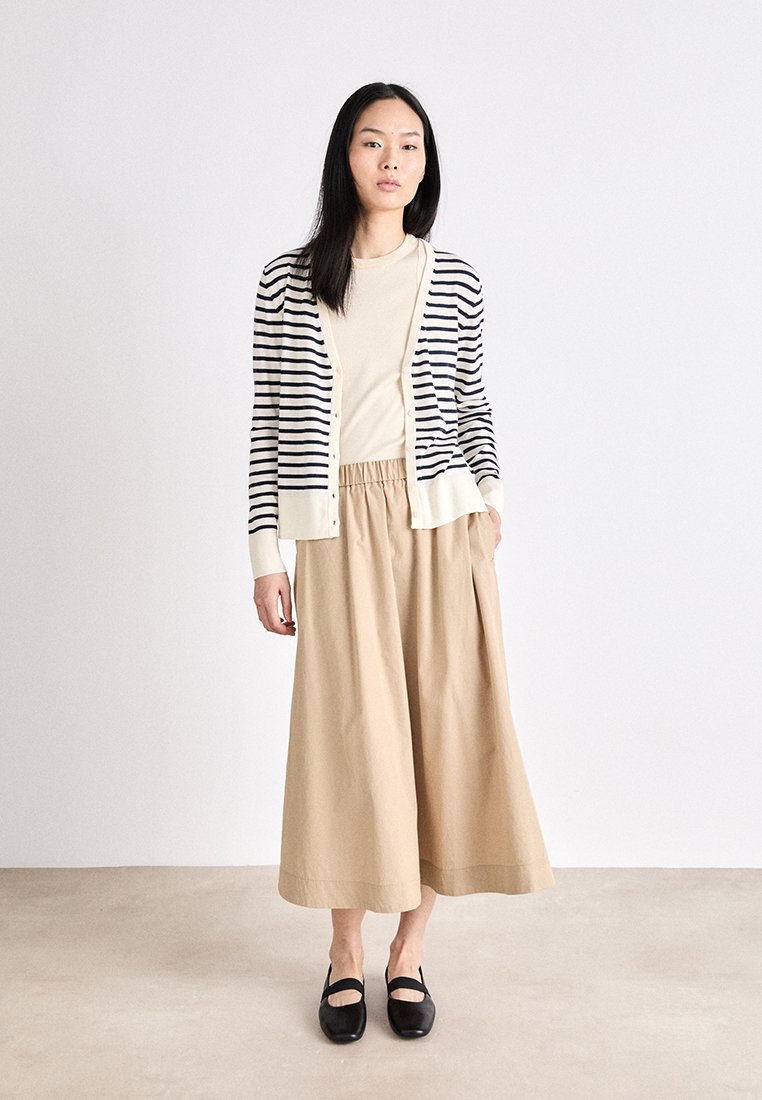 Gestreifter marineblauer und cremefarbener Cardigan, beiger Oberteil und weit geschnittene beigen Hosen, kombiniert mit schwarzen Mary-Jane-Schuhen. Glatte Texturen und lockere Passform.