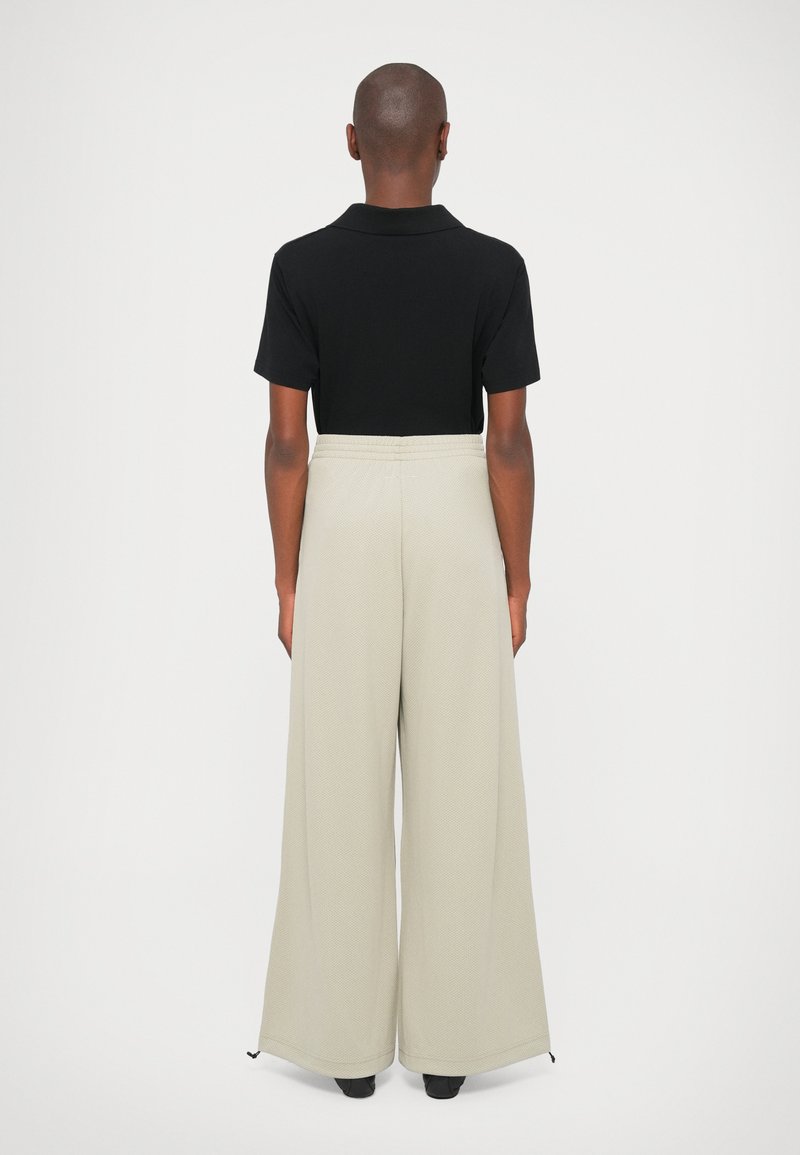 Polo shirt noir à manches courtes associé à un pantalon large beige clair avec un motif texturé et une taille élastique.