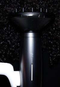 Sèche-cheveux noir ghd speed avec embout diffuseur séchant des cheveux bouclés noirs serrés sur fond noir.