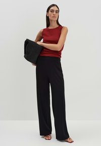 Top rosso senza maniche, pantaloni neri a palazzo e borsa intrecciata nera; sandali in una tonalità nude. Texture liscia con un design aderente.