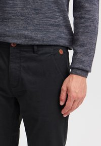 Sorte chinos laget av bomull med en glatt tekstur, med en brun lærlogo og knappelukking. Strikket genser i marineblå farge.