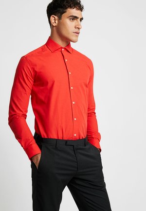 Camisa roja de manga larga con botones y cuello clásico, con una textura suave y botones blancos, combinada con pantalones negros.