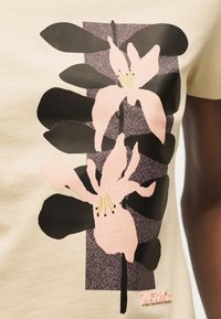 Κάθετο λουλουδένιο σχέδιο σε μπεζ ύφασμα με ανοιχτό ρόζ κρίνα και σκούρα καφέ φύλλα, επάνω σε υφασμάτινο μοτίβο σε μοβ ορθογώνιο.