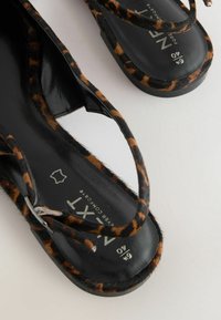 Sandales en cuir noir avec des brides à imprimé léopard, semelles plates et finition texturée. Présente un logo de marque sur la semelle intérieure.
