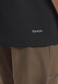 Maglietta nera a maniche corte realizzata in tessuto leggero con una texture liscia, caratterizzata da un piccolo logo argento "TEXADRI" sull'orlo.