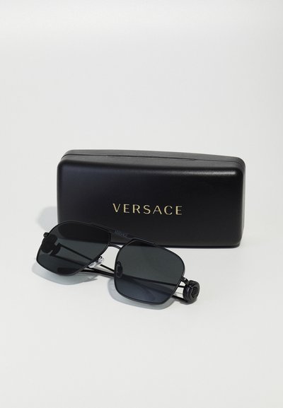 Lunettes de soleil Versace avec des verres rectangulaires noirs et une monture en métal, arborant le logo sur les branches, accompagnées d'un étui noir avec des inscriptions dorées.