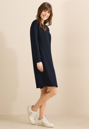 Navyblauwe jurk met lange mouwen, losse pasvorm, gemaakt van zacht materiaal, net boven de knie, gecombineerd met witte en grijze sneakers. Eenvoudig ontwerp, geen patronen.