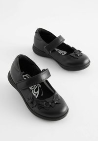 Chaussures Mary Jane en cuir noir avec une sangle, ornées de décorations en forme de papillon et d'une texture lisse. Conception à semelle plate.