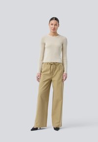 Beige ribbed long-sleeve top paired with loose-fitting beige trousers featuring a drawstring waist, set against a light gray background.