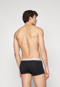 Svarte bomullsboxershorts med et lysegrått elastisk liv, vist fra baksiden på en person med krøllete hår og en nøytral bakgrunn.