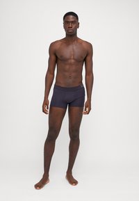 Dunkelviolette Schwimmshorts mit tailliertem Schnitt, hergestellt aus glattem, dehnbarem Stoff. Verfügt über einen Bund mit einem Logodetail.