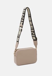 Béžová obdélníková taška z texturované kůže. Má zlatý zip a černo-krémový pruhovaný nastavitelný popruh s logem.