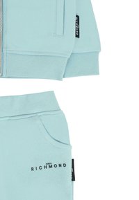 Jasnoniebieski zestaw swetra i spodni, z mankietami ribbed, zamek błyskawiczny oraz logo na obu elementach. Gładka tekstura, luźny krój.