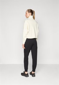 Kuttet kremfarget sweatshirt med høy krage, lagt sammen med svarte joggebukser og svarte joggesko, med elastiske mansjetter og avslappet passform.