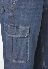 Denim cargo pants in dark blue with a textured finish, featuring a large side pocket and stitch detailing along the seams.