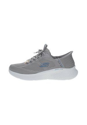 Chaussure de sport grise avec empeigne en maille, texture surélevée, design à lacets et semelle blanche. Présente des détails de logo et de marque subtils.