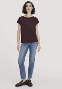 Burgunderfarbener T-Shirt mit kurzenÄrmeln und Rundhalsausschnitt, kombiniert mit hellblauen Schlagjeans und dunkelbraunen geflochtenen Slippern.