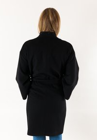 Cappotto nero con cintura, maniche lunghe, colletto alto e texture liscia. Design semplice senza motivi o hardware visibili.
