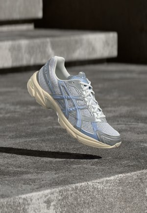 Chaussure de course blanche et bleu clair flottant au-dessus d'une surface en béton avec des marches en pierre en arrière-plan.