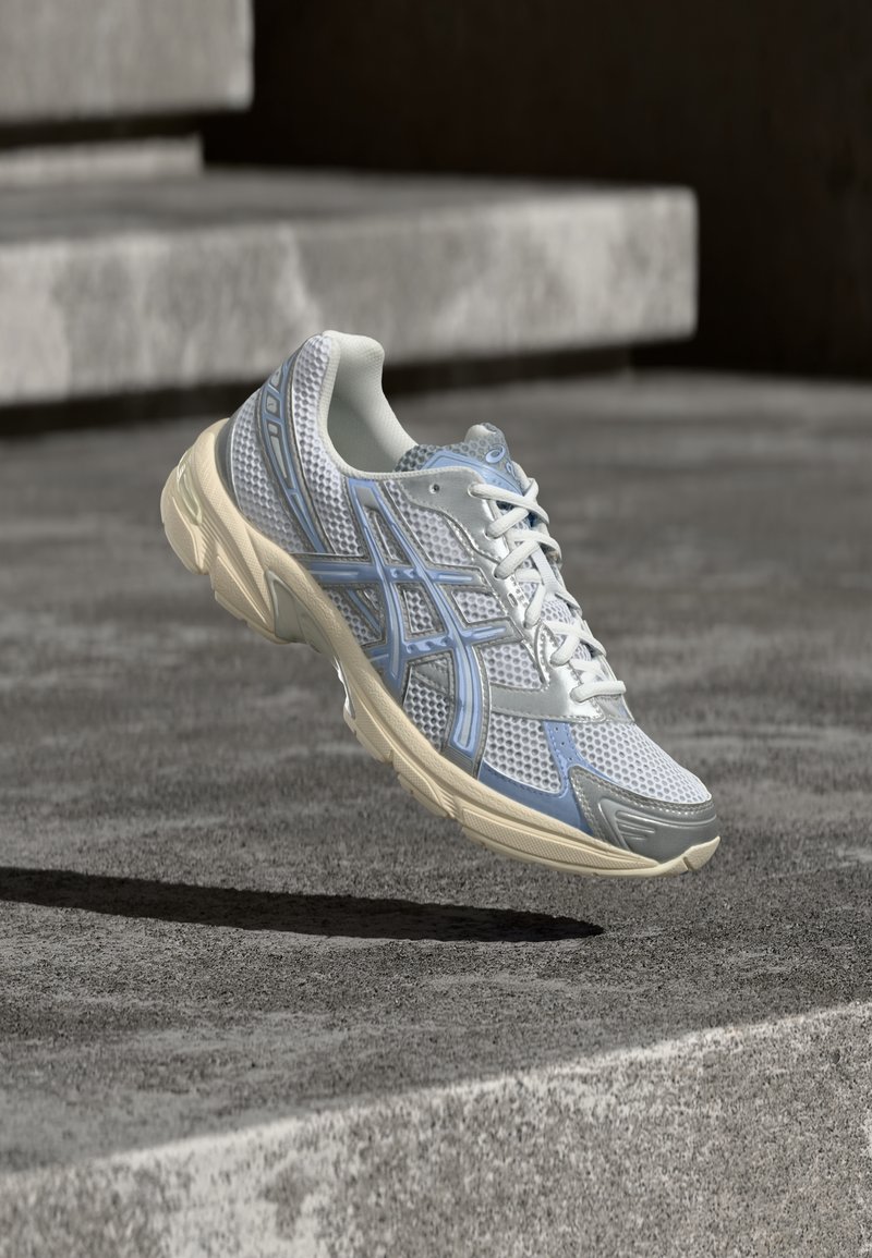 Chaussure de course blanche et bleu clair flottant au-dessus d'une surface en béton avec des marches en pierre en arrière-plan.