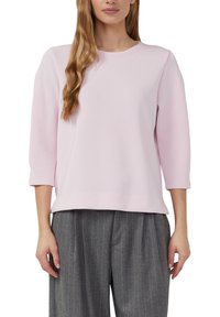 Hellrosa Sweatshirt aus Baumwollmischung mit Rundhalsausschnitt und dreiviertellangen Ärmeln, kombiniert mit grauen, fein gestreiften Hosen. Glatte Textur.