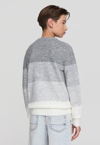 Szary sweter w gradientowym wzorze, wykonany z miękkiego materiału, z białymi mankietami i wykończeniem. Tył swetra ma gładki, subtelny wzór pasków przechodzących od ciemnoszarego do jasnoszarego.