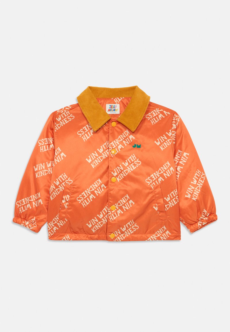 Oranžinė satino striukė su velveto apykakle, ant kurios kartojasi tekstas "LAIMĖK SU GERUMU" baltos spalvos, ir geltonos sagos. Pulsuojantys rankogaliai.