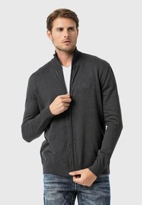 Dunkelgrauer Reißverschluss-Pullover mit hohem Kragen, gerippten Bündchen und Saum, kombiniert mit einem weißen T-Shirt und blauen Jeans. Sanfte Textur.