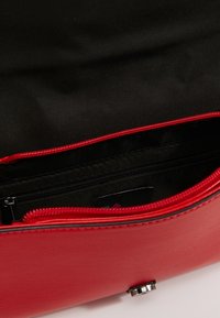 Wnętrze czerwonej skórzanej torebki z czarnym materiałem wykończeniowym. Zawiera kieszeń na zamek błyskawiczny i polerowane akcesoria. Gładka tekstura, strukturalny design.