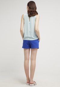 Canotta azzurra, leggera, con uno spacco sul retro, abbinata a pantaloni corti blu e sandali bianchi; tessuti morbidi e vestibilità comoda.