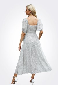 Witte jurk met zwarte stippen, korte pofmouwen, getailleerde bodice, vierkante rug en een vloeiende rok die tot halverwege de kuit reikt.