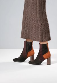 Stivaletti alla caviglia con pannelli multicolore in suede nero, bordeaux e arancione, con tacco a blocco in legno e dettaglio con cerniera laterale.