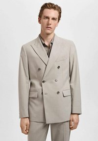 Giacca da abito beige doppiopetto con revers a punta, due tasche frontali e dettagli con bottoni, realizzata in un tessuto liscio e testurizzato.