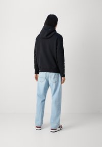 Svart huvtröja med avslappnad passform, kombinerad med ljusblå jeans och vinröda och vita sneakers. Enkel, samtida design.