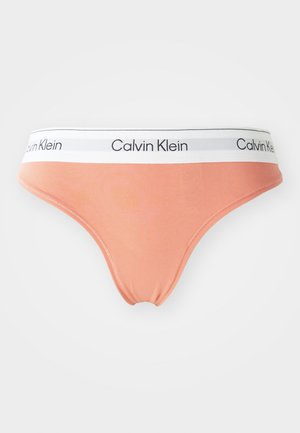 Tanga color durazno de Calvin Klein con cinturilla elástica blanca que presenta la marca en negro. Tejido suave con bordes lisos y un ajuste elástico.