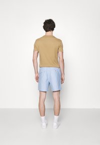 Avslappnad outfit med en ljusbrun t-shirt med kort ärm och ljusblå shorts med två bakfickor, kombinerat med vita sneakers och strumpor.