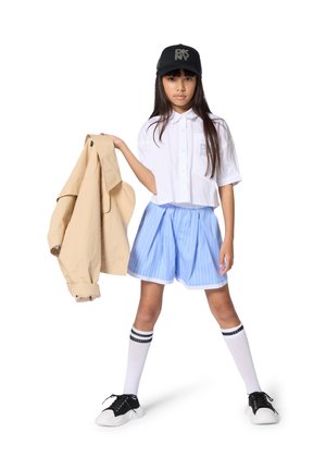 Witte cropped blouse met knopen en lichtblauwe pinstripe korte broek, beige jas, zwarte pet, gestreepte sokken en zwarte sneakers met witte zolen.